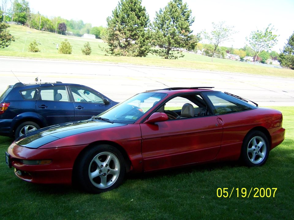 Red 1996 Ford Probe parked on grass next to a blue SUV