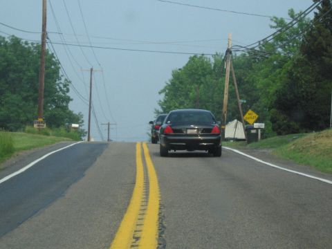 1991 Ford LTD Crown Victoria - Two sedans travel down a rural road with power lines overhead and trees lining the sides.