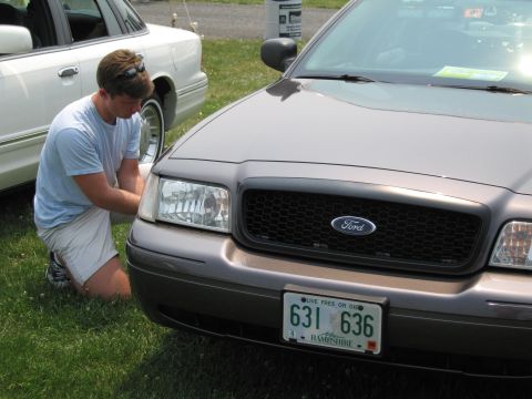 1991 Ford LTD Crown Victoria - A man works on the headlight of a dark gray Ford Crown Victoria, with another Crown Victoria nearby.