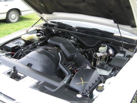 1991 Ford LTD Crown Victoria - The engine bay of a white vehicle is shown with the hood open. A second vehicle is visible in the background.