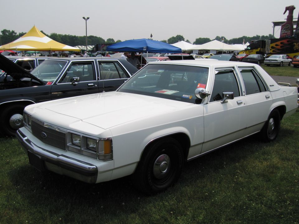 White 1980s Ford sedan parked on grass, another car visible behind it