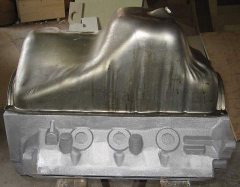 1972 Ford Ranchero - Bare V8 engine block sitting upside-down on wood blocks with a stamped-steel oil pan still bolted in place, both stripped to bare metal aft…