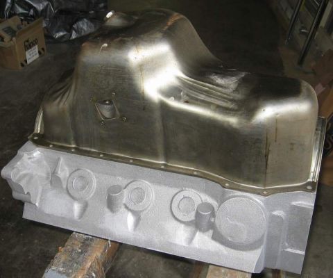 1972 Ford Ranchero - A bare, unpainted cast engine block sits on wood blocks with a raw sheet-metal deep-sump oil pan resting on top, showing bare machined surf…