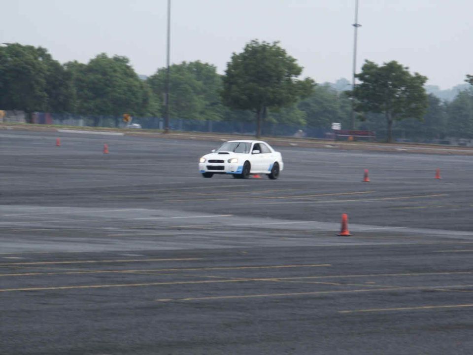 White Subaru WRX STI with blue accents on a wet asphalt course with orange cones