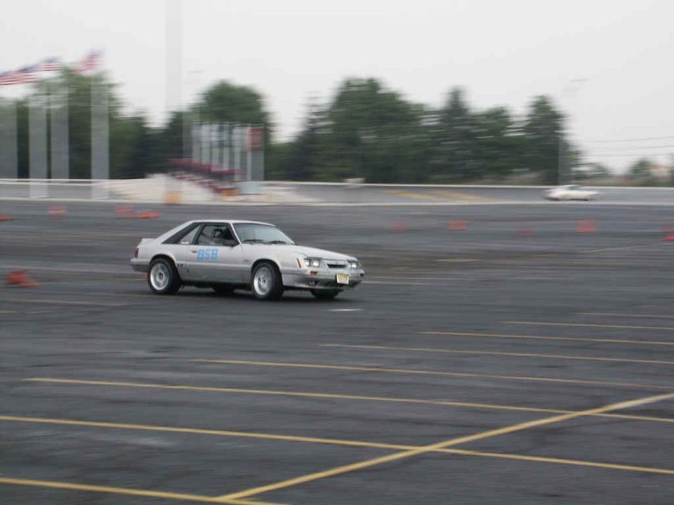 Silver coupe with "ASB" text on door, driving on asphalt track with orange cones