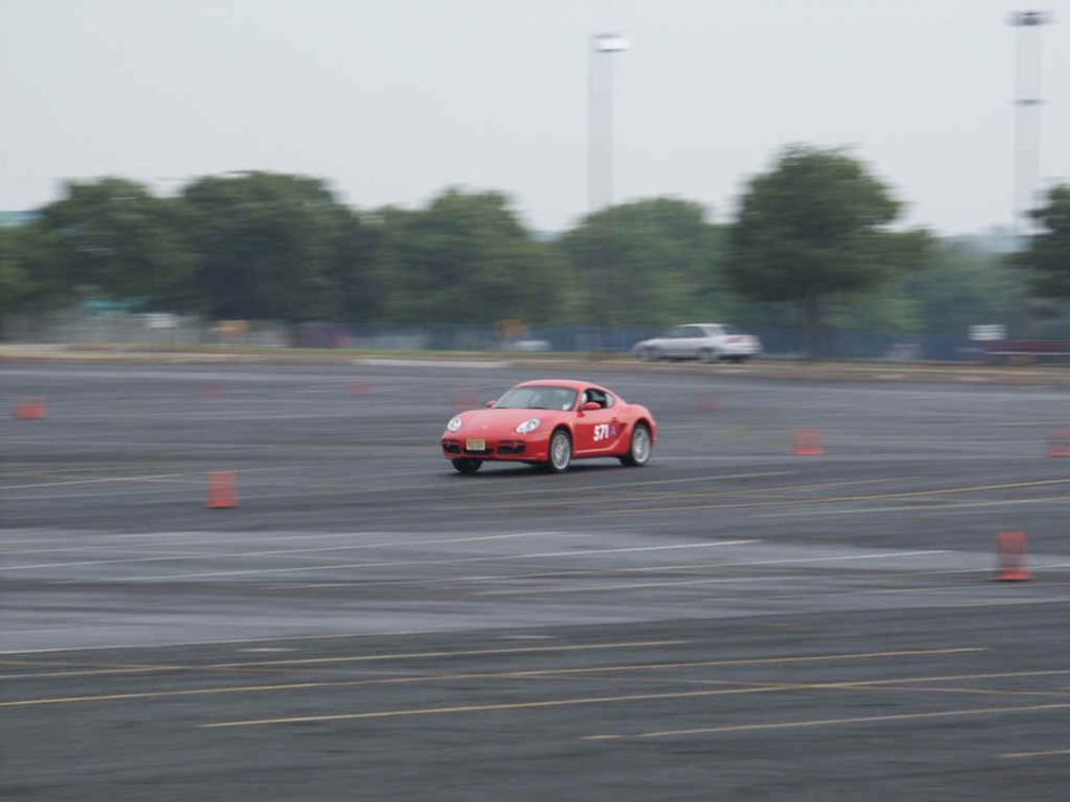 Red sports car with number 371 on the side driving on a paved track with orange cones