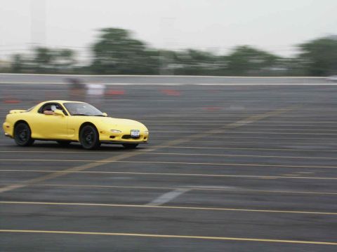 2001 Mercury Grand Marquis - A yellow Mazda RX-7 is captured in motion on a paved surface with lane markings.