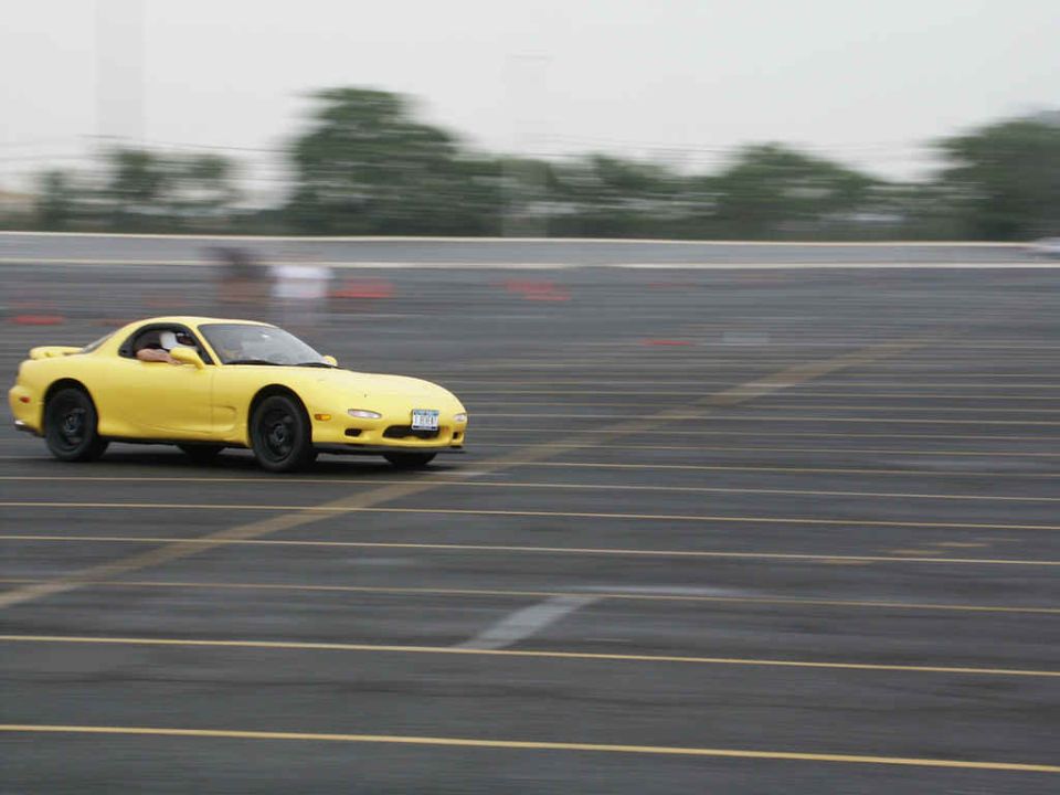 Yellow Mazda RX-7 driving on a track, driver visible inside