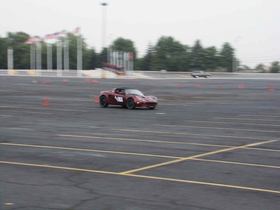 Red sports car with number 53 on door driving on asphalt track with orange cones