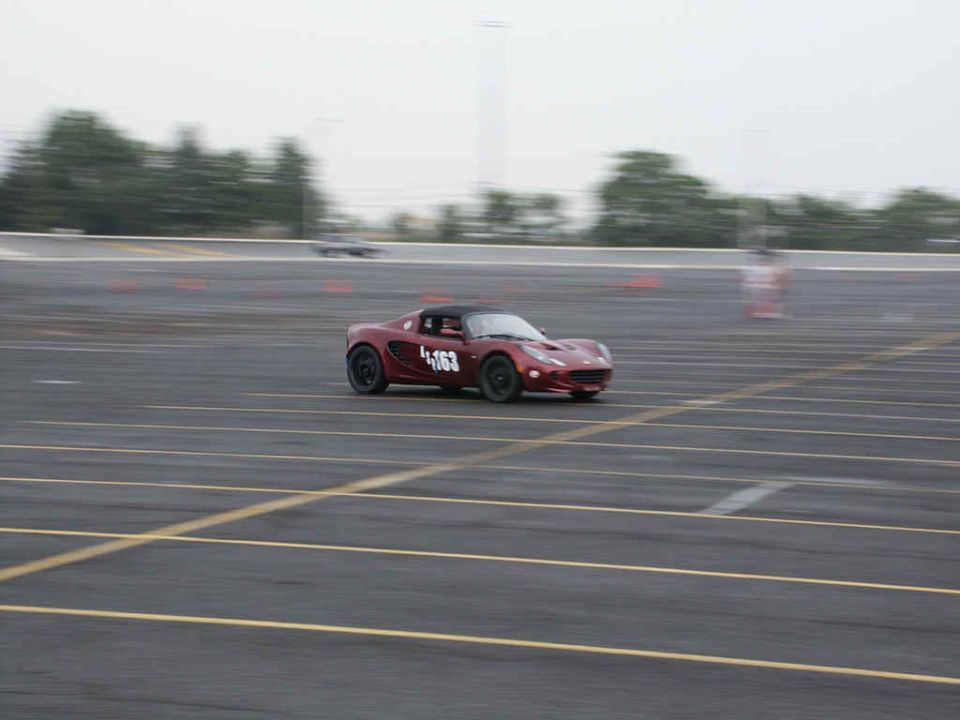 Red sports car with number 163 on door driving on a paved track with orange cones