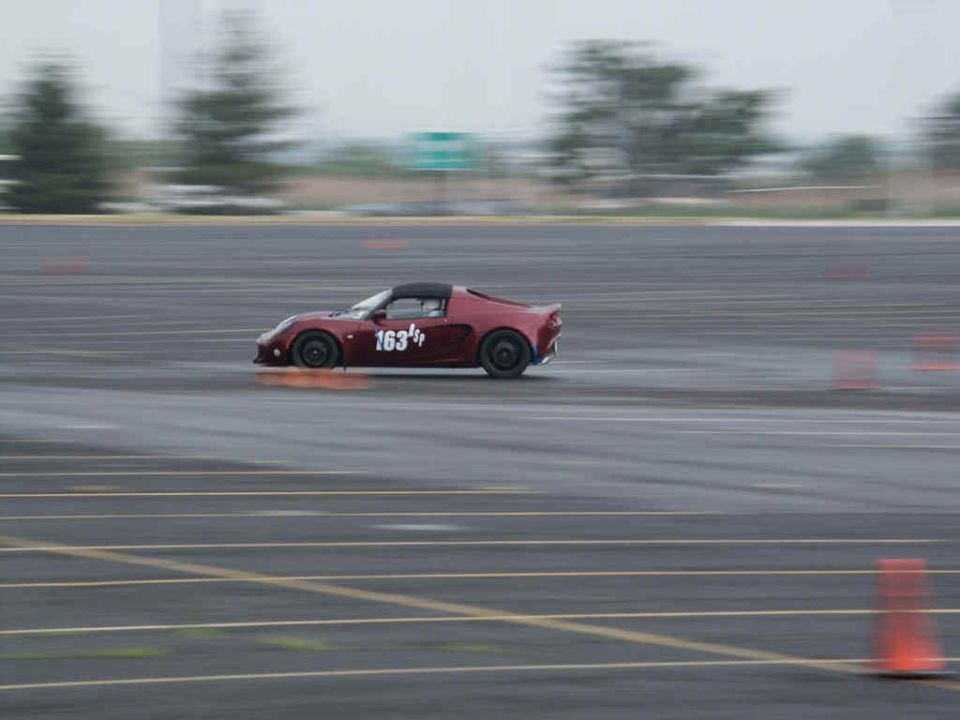 Red sports car with number 163 on door driving on a wet track with orange cones