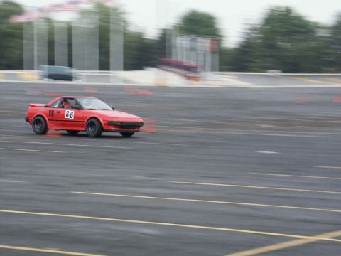 2001 Mercury Grand Marquis - A red sports car with racing number 86 is captured in motion on a paved track, with cones visible.