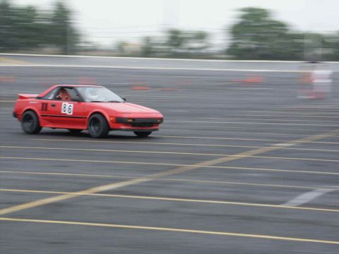 2001 Mercury Grand Marquis - A red sports car with racing numbers is captured in motion on a paved track.