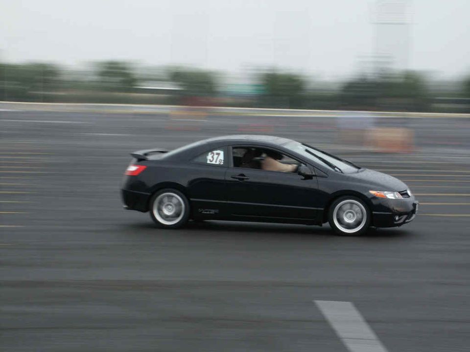 black coupe with racing number 37 on door, moving fast on wet asphalt track