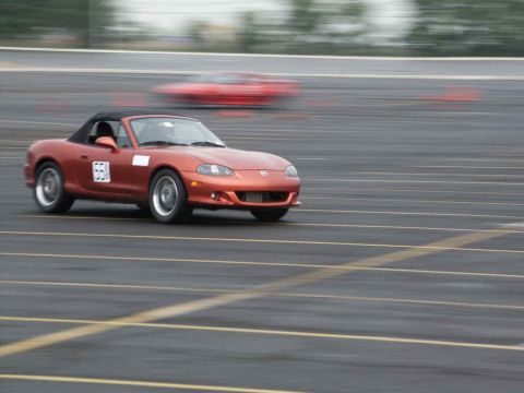 2001 Mercury Grand Marquis - Orange convertible sports car navigates a track with another blurred vehicle in the background.