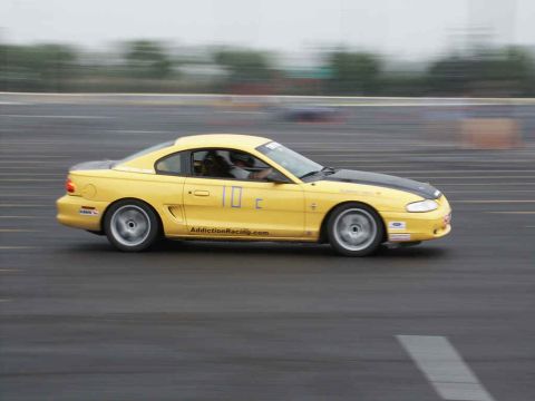 2001 Mercury Grand Marquis - A yellow Ford Mustang with a black hood races on a track, showing motion blur.