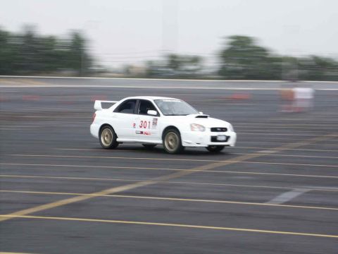 2001 Mercury Grand Marquis - A white Subaru Impreza WRX with racing decals navigates a track, captured with motion blur.