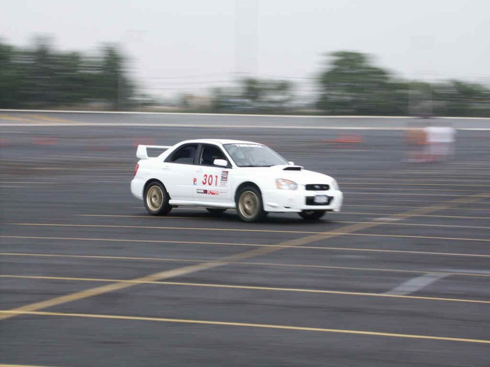 White Subaru Impreza WRX with racing decals, driving on a track