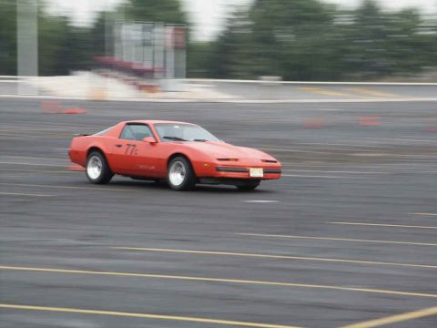 2001 Mercury Grand Marquis - Orange Pontiac Firebird with "77c" on door driving on asphalt track during an event.