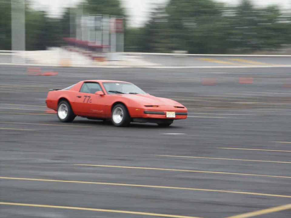 Orange Pontiac Firebird with "77c" on door driving on asphalt track