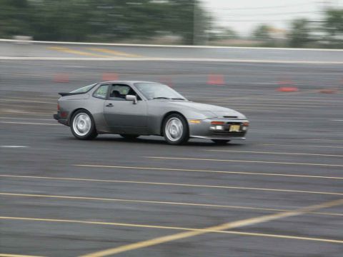 2001 Mercury Grand Marquis - A gray Porsche 944 is captured in motion on a paved track with orange cones visible in the background.