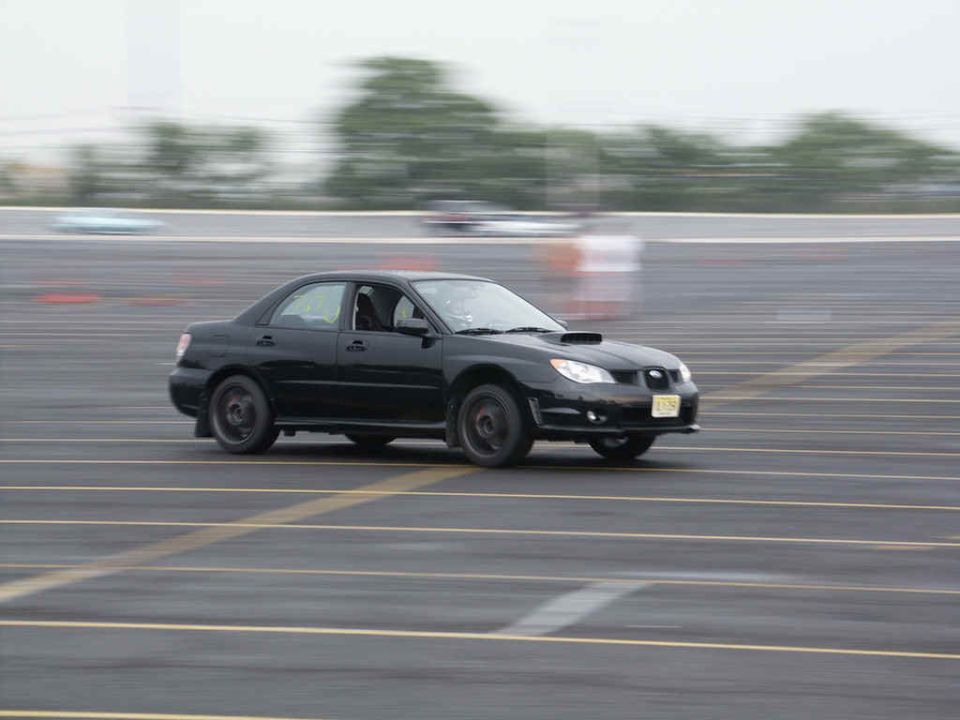 Black Subaru Impreza WRX sedan with hood scoop driving on a track