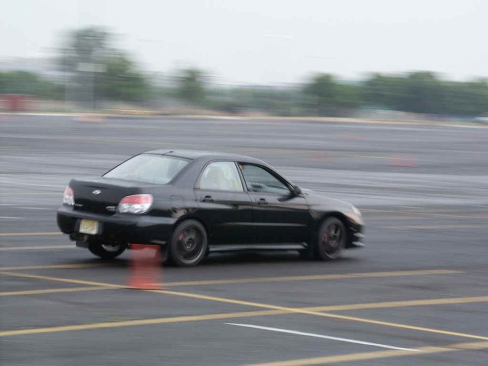 Black sedan doing a turn on a track, cones visible