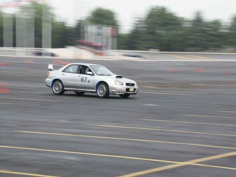 2001 Mercury Grand Marquis - Silver Subaru Impreza WRX STI with racing number 67 navigates a track, blurred by motion.