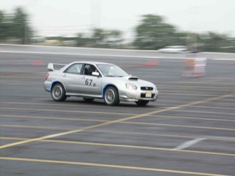 2001 Mercury Grand Marquis - Silver Subaru WRX STI with racing number 67b on door, driving on asphalt track.