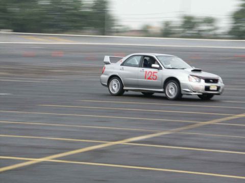 2001 Mercury Grand Marquis - A silver Subaru WRX STI with a racing number is captured in motion on a paved track with orange cones visible.