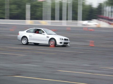 2001 Mercury Grand Marquis - A silver coupe with racing number 100 navigates a course marked by orange cones, with another vehicle blurred in the background.