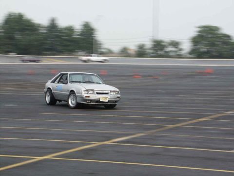 2001 Mercury Grand Marquis - A silver Ford Mustang is seen on a paved track with orange cones marking a course.