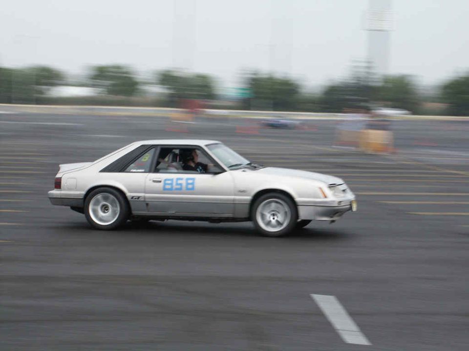 Silver 1987 Ford Mustang GT coupe with blue racing number 858 on the door, seen from the side in motion
