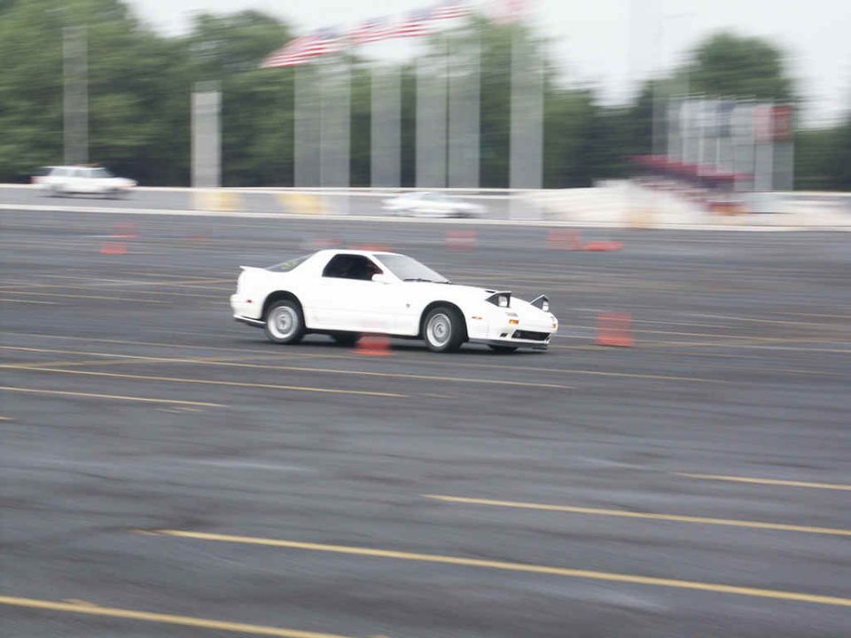 White sports car with pop-up headlights driving on a track with orange cones