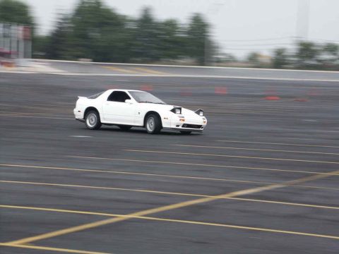 2001 Mercury Grand Marquis - A white sports car is captured in motion on an asphalt track with orange cones in the background.
