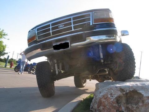 1996 Ford Bronco - A lifted Ford Bronco is positioned on large rocks, showing its front end and modified suspension.