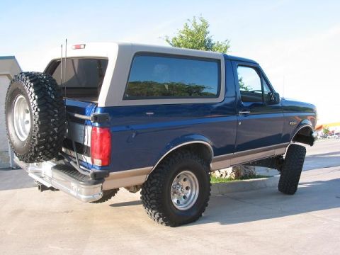 1996 Ford Bronco - This lifted 1996 Ford Bronco features a blue exterior, a tan removable top, and a spare tire mounted on the rear tailgate.