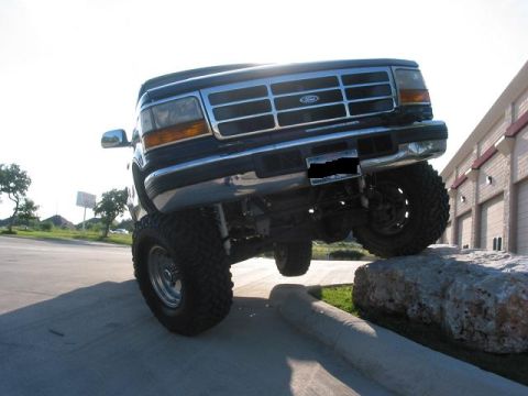 1996 Ford Bronco - This lifted Ford Bronco is positioned on rocks, showing its front grille and off-road tires.