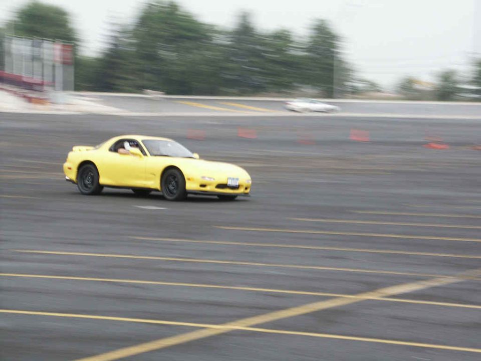 Yellow sports car with black wheels on a track, driver visible, motion blur
