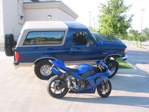 1996 Ford Bronco - A blue sportbike is parked in front of a blue Ford Bronco SUV, with a spare tire mounted on the rear of the SUV.
