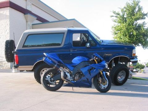 1996 Ford Bronco - A blue Ford Bronco and a blue sport motorcycle are parked side-by-side in a lot.