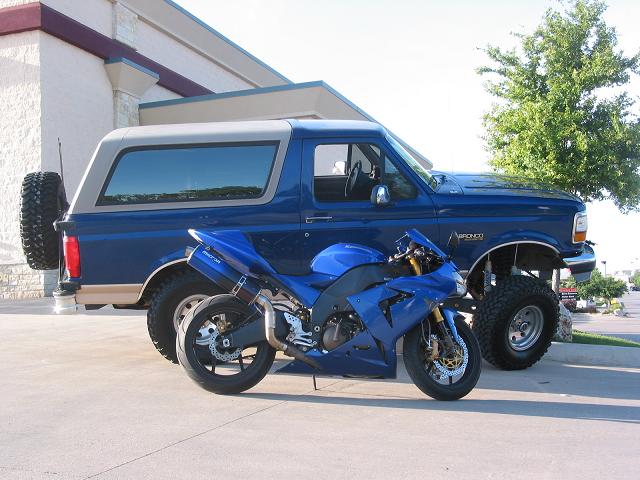 Blue Ford Bronco with lifted suspension and off-road tires, parked next to a blue sport motorcycle