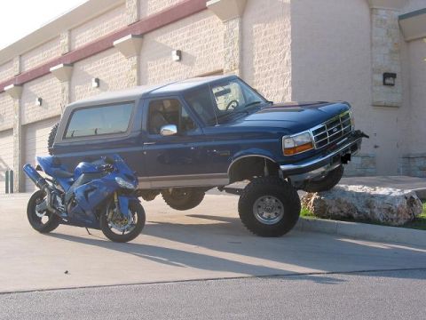 1996 Ford Bronco - A blue 1996 Ford Bronco is parked next to a blue motorcycle on a paved surface.