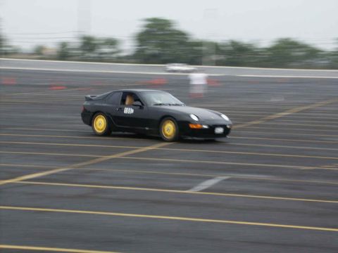 2001 Mercury Grand Marquis - A black sports car with distinctive yellow wheels navigates a wet track during an event.