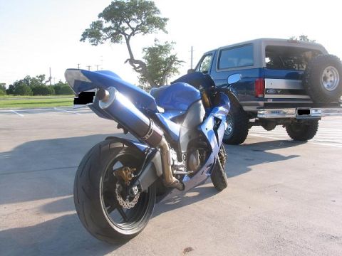 1996 Ford Bronco - A blue sportbike is parked in front of a blue Ford Bronco, with the Bronco's spare tire mounted on the rear.