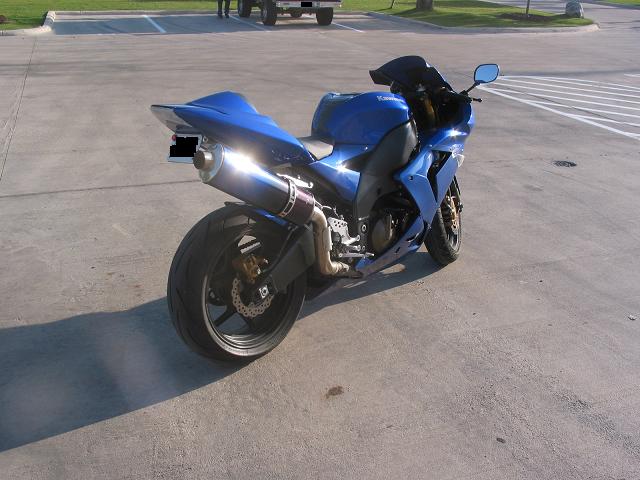 Blue Kawasaki motorcycle parked on concrete, rear three-quarter view