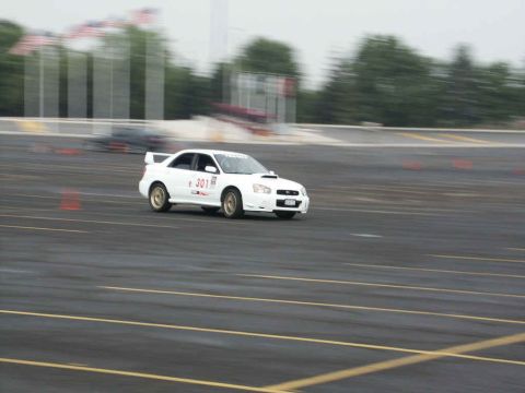 2001 Mercury Grand Marquis - White Subaru WRX STI competes on a race track, with another car blurred in the background.