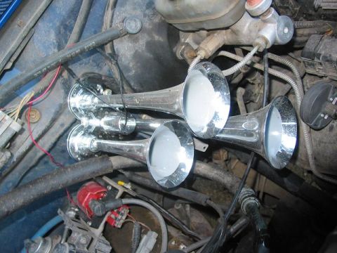1996 Ford Bronco - Close-up of multiple chrome train horns installed in a vehicle's engine compartment.