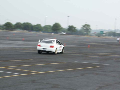 2001 Mercury Grand Marquis - A white sedan with a prominent rear spoiler navigates a cone course on a cloudy day.