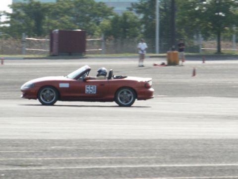 2001 Mercury Grand Marquis - Red convertible sports car on a track, driver wearing a helmet and racing number 55 visible.